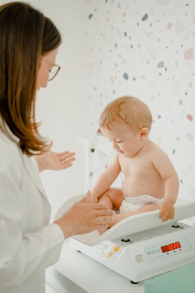 Mother holding baby during vaccination consultation with pediatrician and updated vaccine schedule displayed 