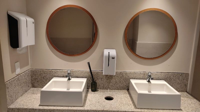 Dispenser de papel toalha aberto durante manutenção com mãos segurando peças e ambiente limpo e bem iluminado 