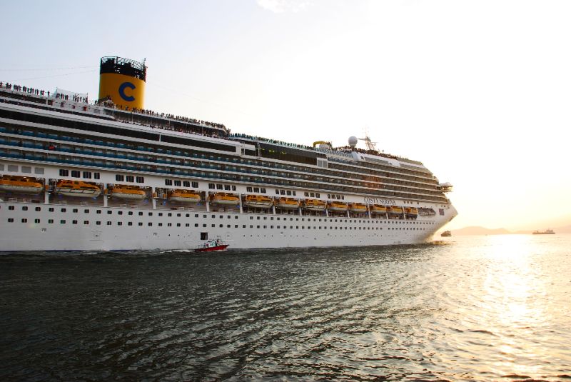 Navio de cruzeiro Costa Serena navegando em mar calmo ao pôr do sol com céu laranja e azul 