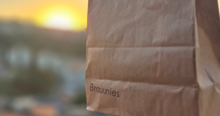Brownies artesanais premium cortados em quadrados, com textura úmida e pedaços brilhantes de chocolate belga, apresentados em uma tábua de madeira rústica com detalhes de cacau em pó e folhas de horte