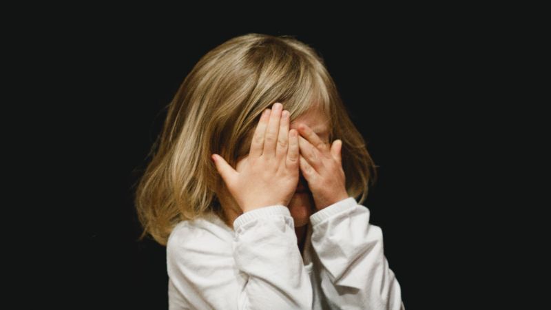 Criança sentada em sofá com expressão preocupada, mãe falando com ela e aconchegando com carinho 