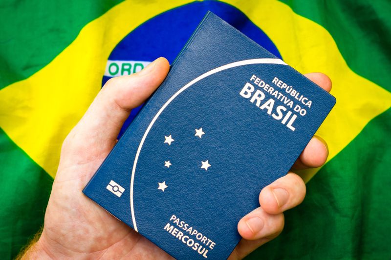 Passaporte brasileiro sobre mesa com logo da Polícia Federal ao fundo e documentos oficiais próximos 