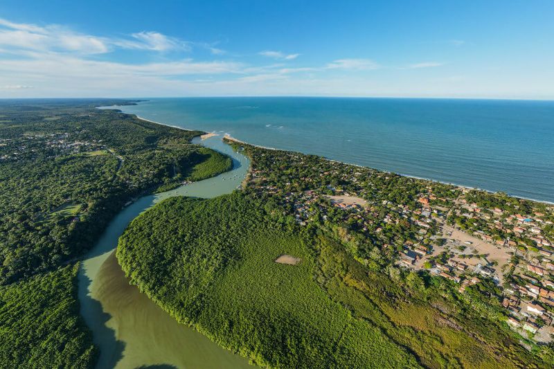 Praia de Caraíva com barcos ancorados no rio e encontro do rio com o mar ao pôr do sol 