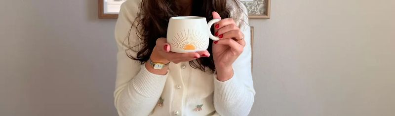 Xícara de café sobre mesa de madeira próxima a janela e livros, ambiente acolhedor com luz natural suave