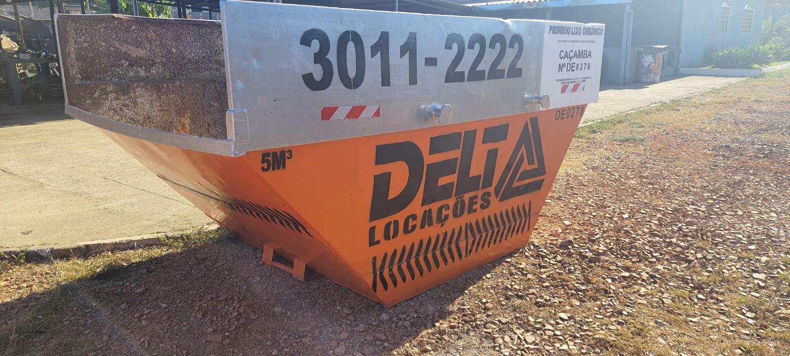 Caminhão posicionando caçamba de entulho em frente a uma obra residencial urbana 