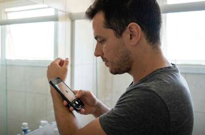 Pessoa fazendo autoexame de pele no espelho com ficha de sinais ao lado 