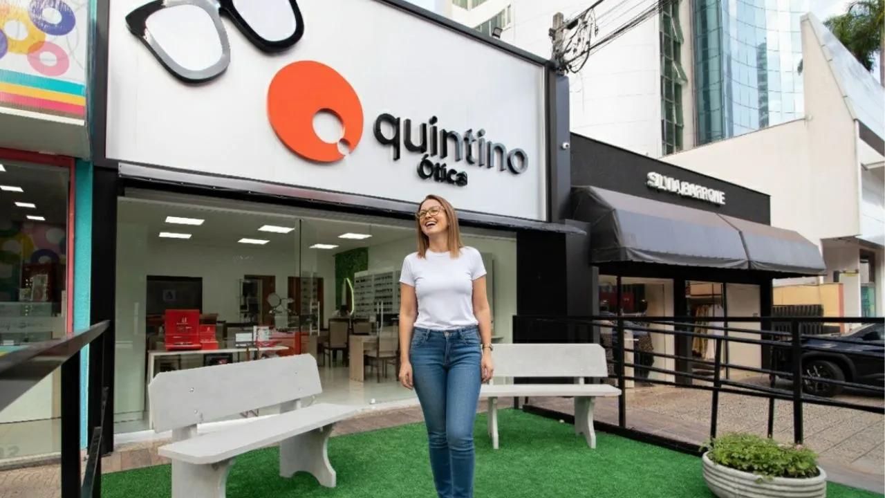 Fachada iluminada de ótica em avenida movimentada de Londrina à noite 